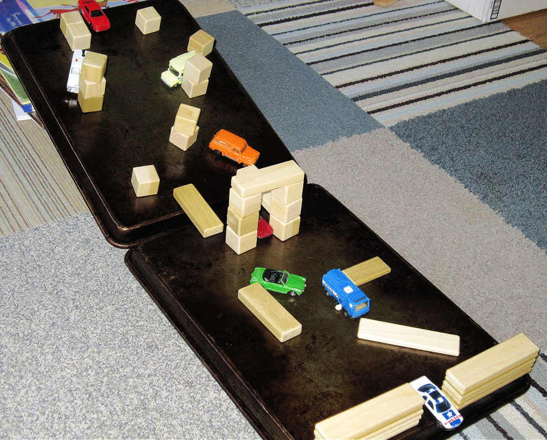 Toy blocks and vehicles on an obstacle course made from baking sheets, on the floor