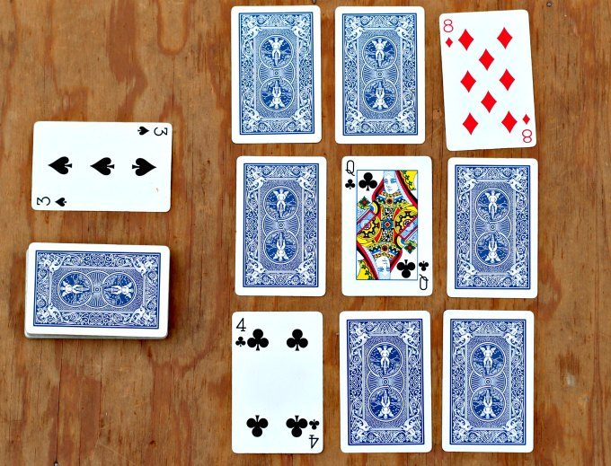 playing card layout of nine cards face up and face down with two extra stacks of cards, on a wooden surface