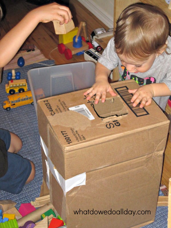 Two children and a cardboard box with a hole in it. 
