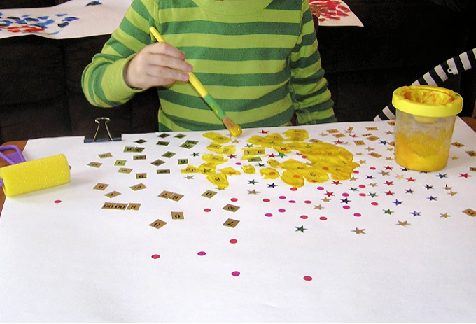 Child painting with yellow paint over stickers