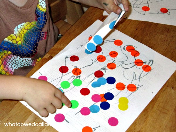 Toddler putting office supply sticker dots on paper. 