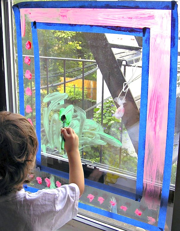 Child painting window glass with washable window paint
